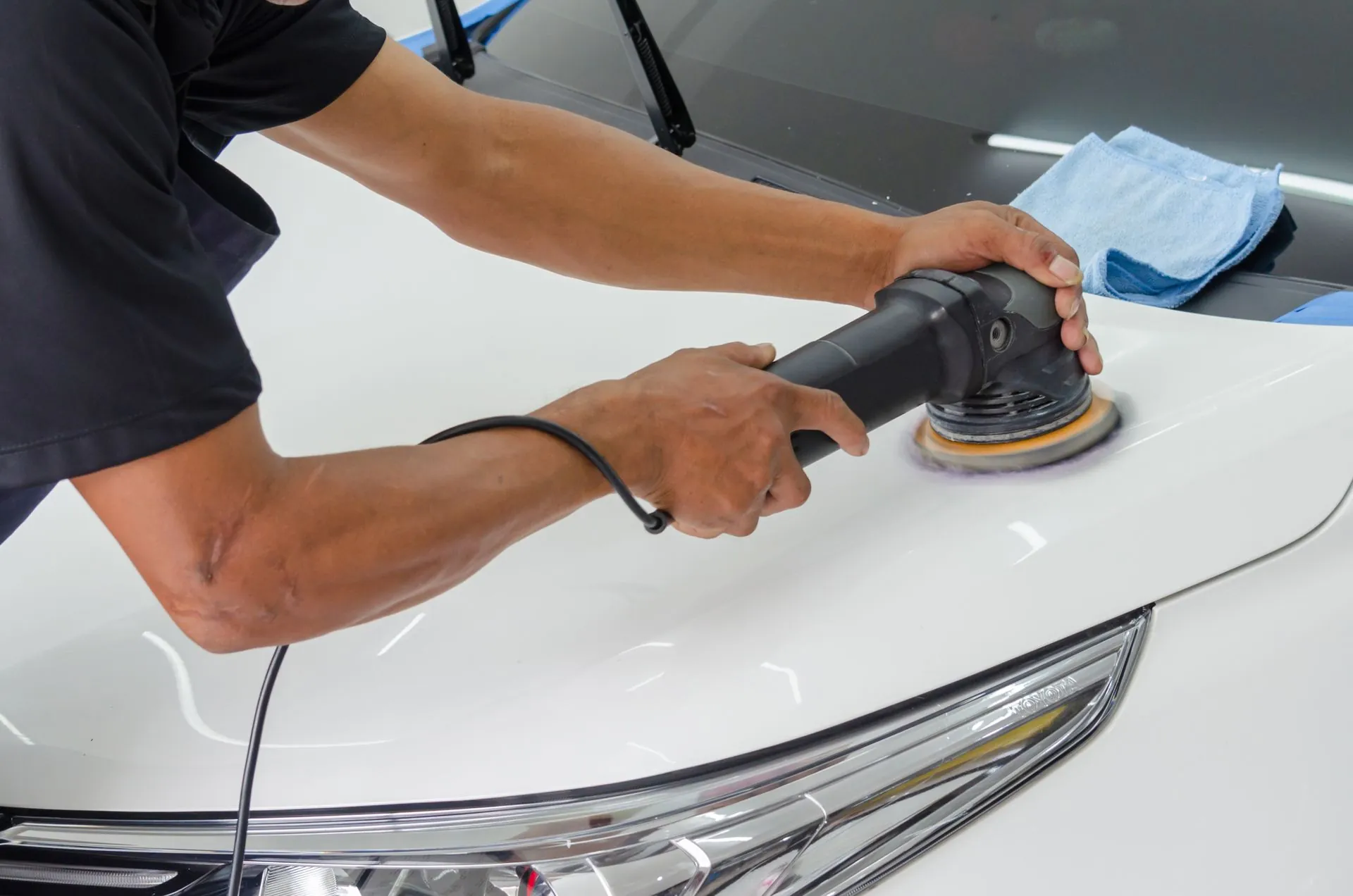 A dual action polisher worked by hand across the bonnet of a white car.
