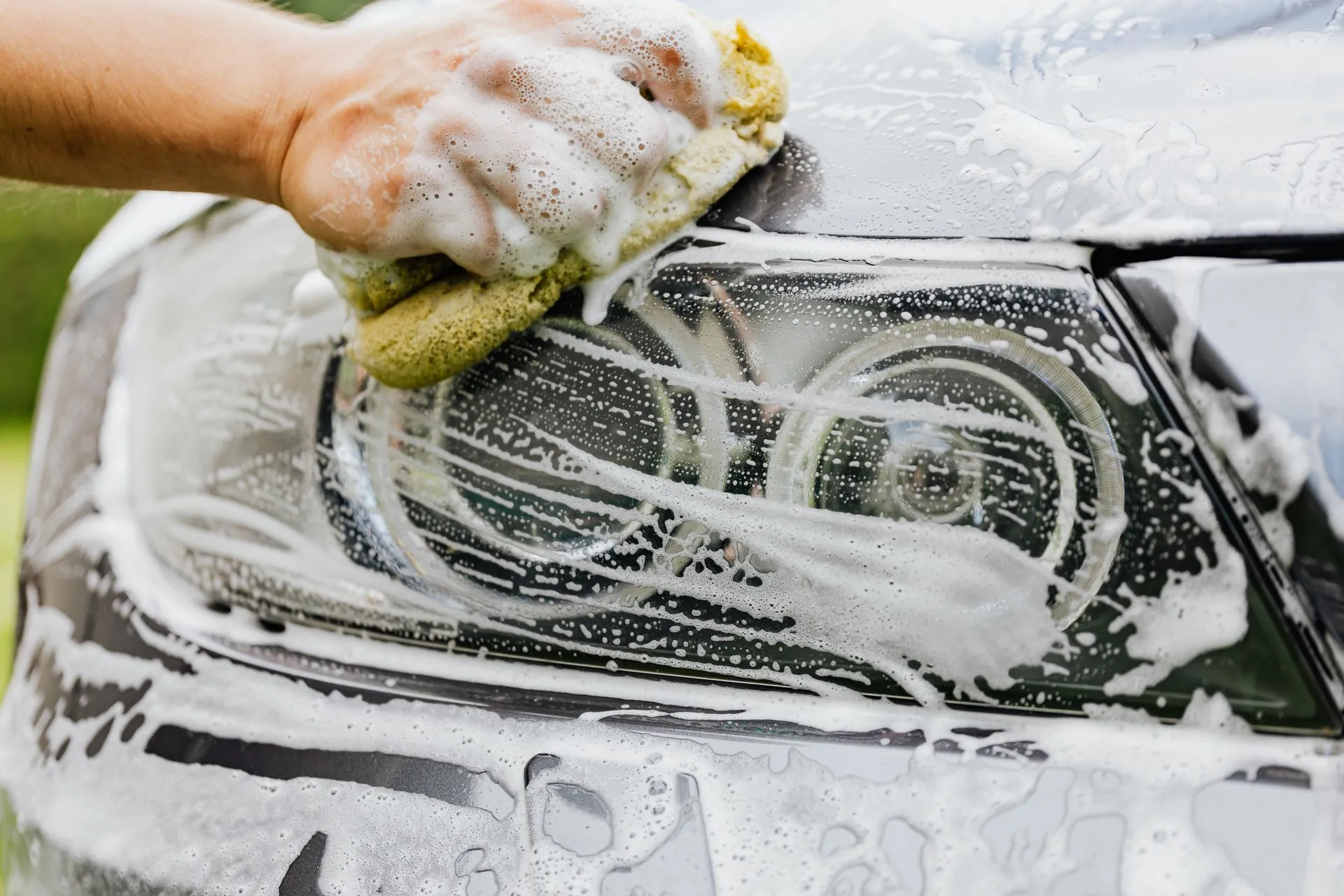A soapy sponge worked by hand across a wheel and headlight.