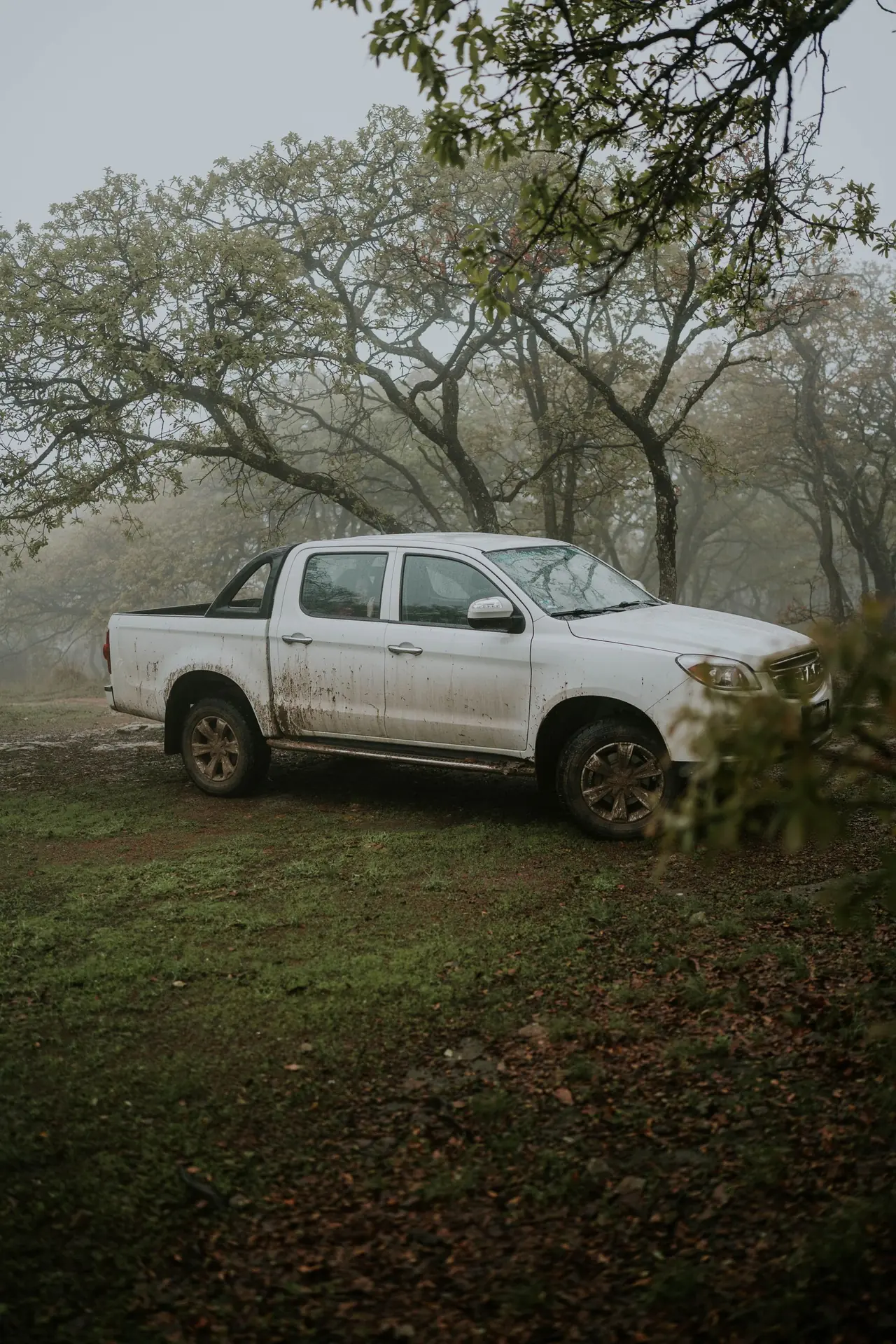 A double cab pickup parked on wet ground, mud splashed up its doors and rear quarter.