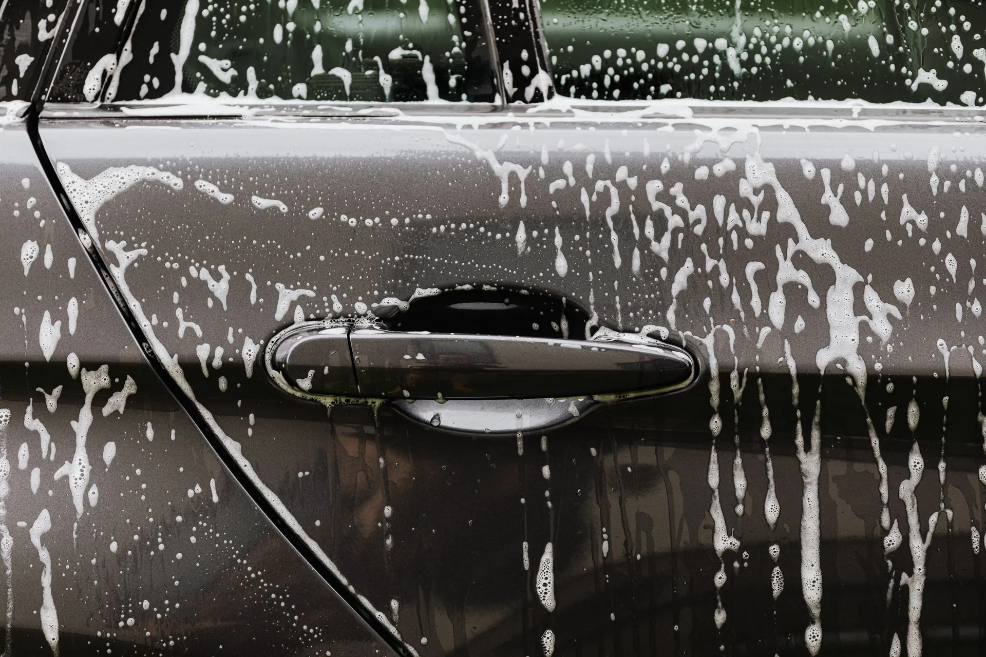 Snow foam running down the door of a dark car.