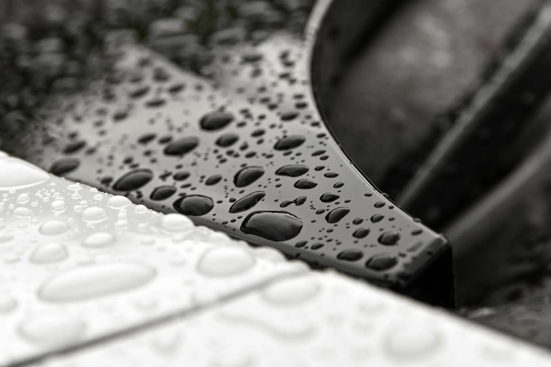 Water beading tightly on a freshly sealed dark car panel.