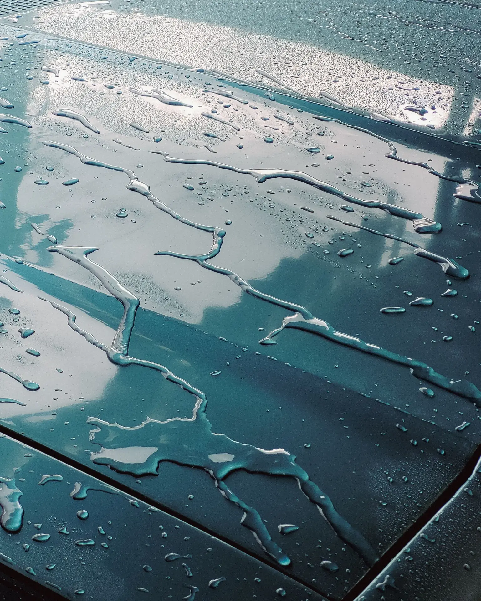 Water running in rivulets across the wet panel of a teal car.